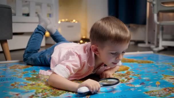 Glücklich lächelnder Junge mit Lupe und Blick auf große Weltkarte. Konzept für Reisen, Tourismus und Kindererziehung. Kinder erkunden und entdecken. — Stockvideo