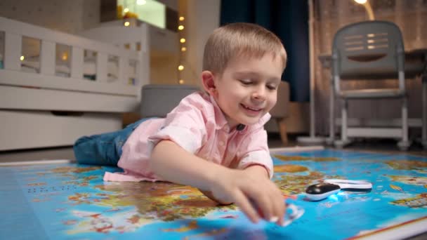 Buon bambino sorridente sdraiato sulla grande mappa e giocare con aeroplano giocattolo. Concetto di viaggio, turismo e educazione dei bambini. Esplorazione e scoperta dei bambini — Video Stock