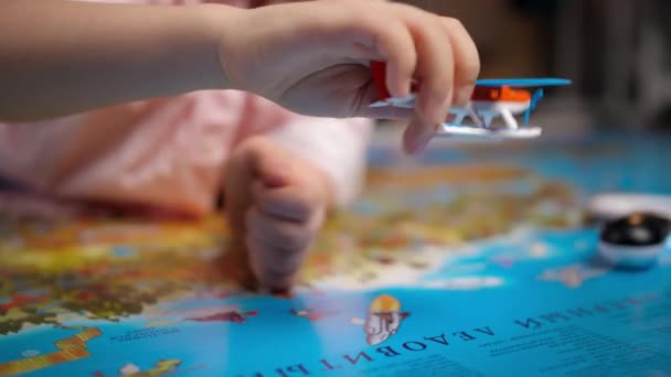Zbliżenie małego chłopca bawiącego się małym samolotem zabawki na wielkiej mapie świata. Pojęcie podróży, turystyki i edukacji dzieci. Dzieci poszukiwanie i odkrywanie — Wideo stockowe