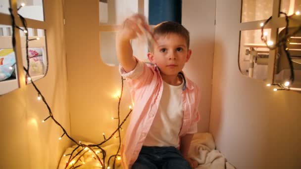 Movimento lento de menino sentado em casa de brinquedo ou tenda tepee e brincando com avião de brinquedo — Vídeo de Stock