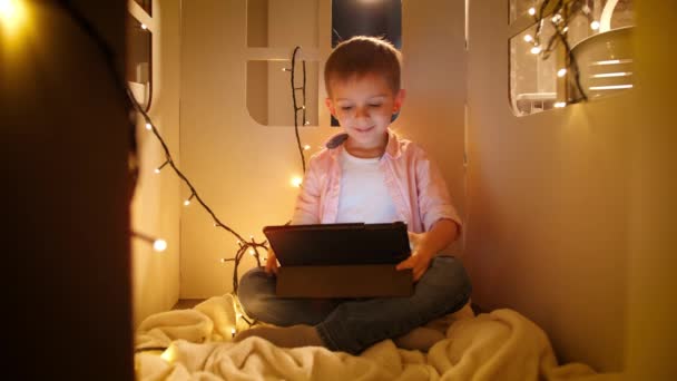 Felice ragazzo allegro sorridente guardare cartoni animati e giochi su tablet computer di notte. Concetto di educazione dei bambini e studio di notte — Video Stock