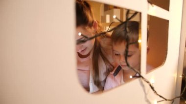 Geceleri küçük bir oyuncak evde küçük oğluna masal kitabı okuyan anne penceresinden bak. Çocuk eğitimi ve aile kavramının geceleri birlikte vakit geçirmesi