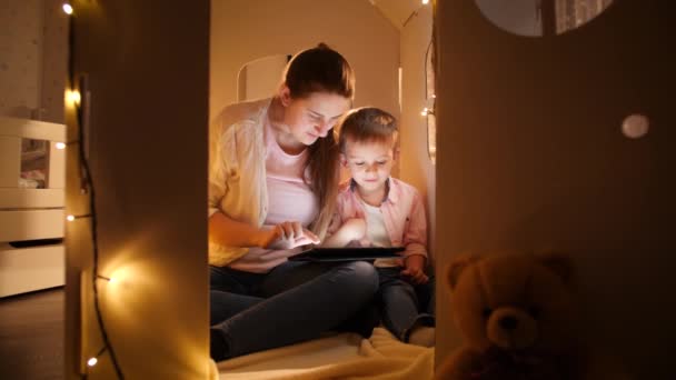 Happy family sitting in tent or toy cardboard house at night and using tablet computer. Concept of child education and family having time together at night — Stock Video