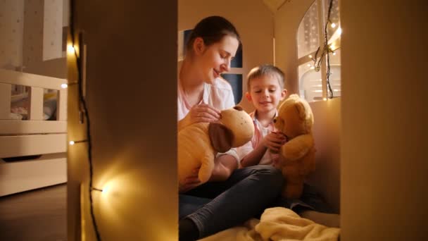 Roztomilý malý chlapec a mladá matka hrát hry s hračkou medvídky v noci ve stanu nebo hračka domu. Koncept dětské hry a rodiny trávit spolu čas v noci. — Stock video