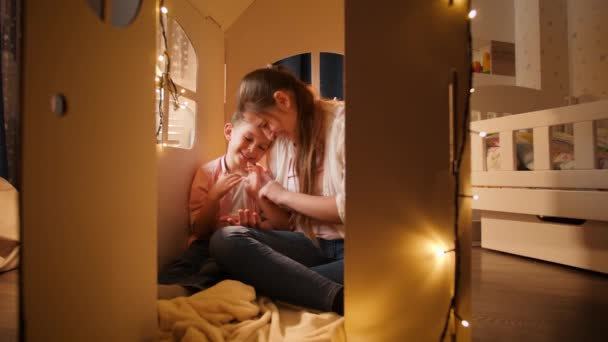 Young loving mother palying with her little son in tent or carboard toy house at night. Concept of child loving parents and family having time together at night. — Stock Video