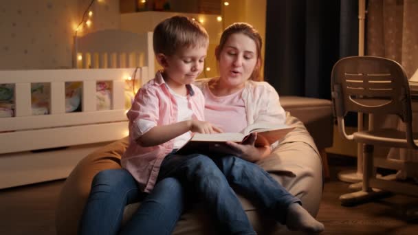 Al rallentatore della giovane madre che legge la favola della buonanotte al suo piccolo figlio prima di andare a dormire. Concetto di educazione dei bambini e famiglia che passano del tempo insieme la notte — Video Stock