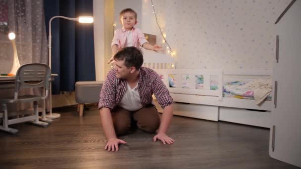 Счастливый улыбающийся отец с маленьким сыном, играющим и верхом на свиньёй в спальне. Концепция игры детей с родителями и семьей, проводящих время вместе ночью — стоковое видео