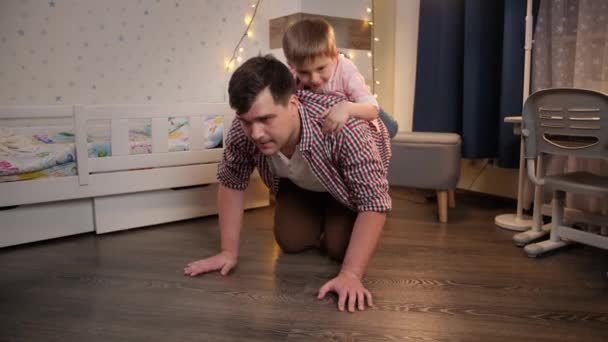 Laughing and cheerful boy riding on his fathers back at night before going to sleep. Concept of child playing with parents and family having time together at night — Stock Video