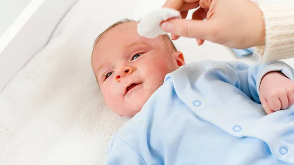 Primer plano de la madre limpiando la cara y los ojos de su hijo recién nacido con almohadilla cooton. Concepto de bebés e higiene y atención sanitaria del recién nacido. Cuidar a los padres con niños pequeños. — Foto de Stock