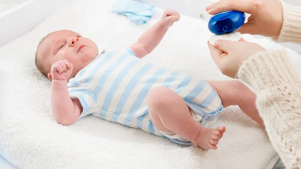 年轻有爱心的母亲用婴儿油对新生婴儿进行保湿、柔软的涂抹，躺在更衣室的桌子上。婴儿和新生儿的卫生和保健概念。养育子女少的父母 — 图库照片