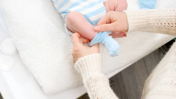 Großaufnahme einer Mutter, die ihren kleinen neugeborenen Sohn anzieht und blaue Socken auf winzigen Füßen anzieht. Konzept der Baby- und Neugeborenenhygiene und Gesundheitsfürsorge. Fürsorgliche Eltern mit kleinen Kindern. — Stockfoto