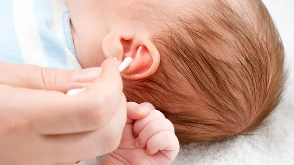耳のワックスから小さな赤ん坊の耳をきれいにするために綿棒を使用して母親の閉鎖。赤ちゃんと新生児の衛生と医療の概念。小さな子供を持つ親の世話. — ストック写真