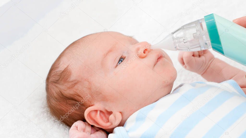 Closeup of mother using electric nasal aspirator to remove mucus from her newborn baby nose. Concept of babies and newborn hygiene and healthcare. Caring parents with little children.