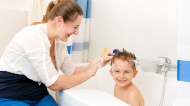 Genç anne oğlunu banyoda yıkıyor ve sabun köpüğüyle ona şık bir saç kesimi yapıyor. Evde çocuk hijyeni ve sağlık hizmetleri kavramı. Aile eğleniyor ve oynuyor..