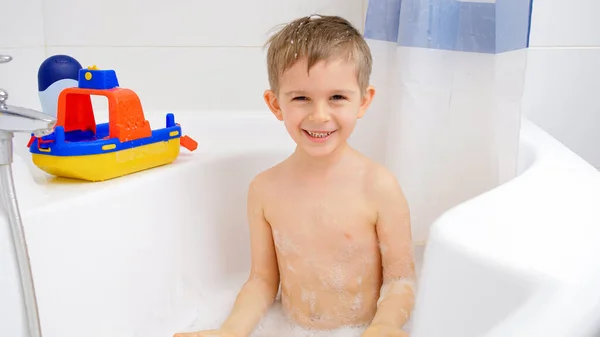 Portrait of cheerful smiling little boy enjoying taking bath with foam. Concept of child hygiene and health care at home — Stock Photo, Image