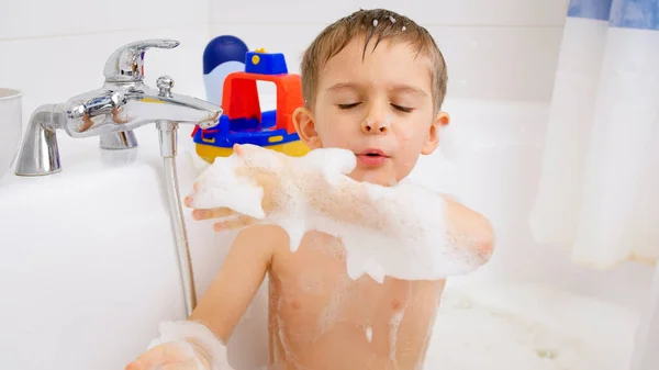 Menino alegre rindo espirrando água e espuma enquanto toma banho. Conceito de higiene infantil e cuidados de saúde em casa. — Fotografia de Stock