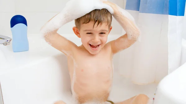 Feliz niño divertido lavándose la cabeza con champú mientras toma un baño en casa. Concepto de higiene infantil y atención sanitaria en el hogar. Niños divirtiéndose y jugando — Foto de Stock