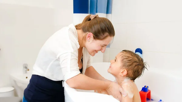 Souriant jeune mère attentionnée laver son petit garçon assis dans le bain avec du savon. Concept d'hygiène infantile et de soins de santé à domicile. Famille avoir du temps ensemble et jouer à la maison — Photo