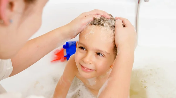 Anne portresi, küçük oğullarının kafasını banyoda şampuanla yıkıyor. Evde çocuk hijyeni ve sağlık hizmetleri kavramı. Aile birlikte vakit geçirir ve evde oynarız. — Stok fotoğraf