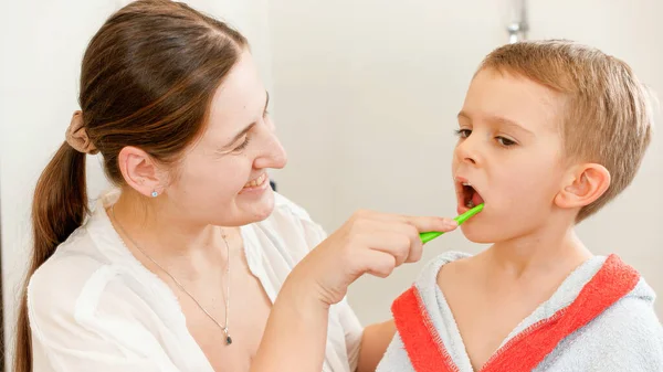 Ung leende mor borsta och rengöra tänderna av sin lilla son med tandborste. Begreppet barntandhygien och hälsovård i hemmet. Vårdande föräldrar och barn hemma. — Stockfoto