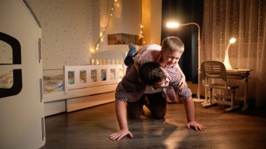 Mutlu gülen küçük çocuk babasının sırtına atlayıp üzerine biniyor. Çocukların aileleri ve aileleriyle oyun oynaması kavramı.