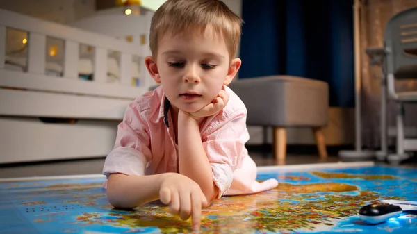 Ritratto di bambino carino che cammina con le dita attraverso la grande mappa del mondo. Concetto di viaggio, turismo e educazione dei bambini. Esplorazione e scoperte per bambini. — Foto Stock