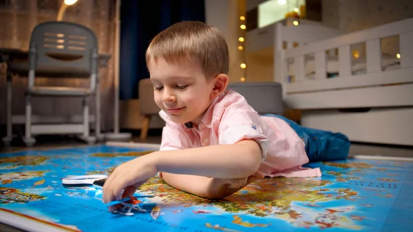 Feliz niño sonriente acostado en un mapa grande y jugando con un avión de juguete. Concepto de viajes, turismo y educación infantil. Exploración y descubrimiento infantil — Foto de Stock