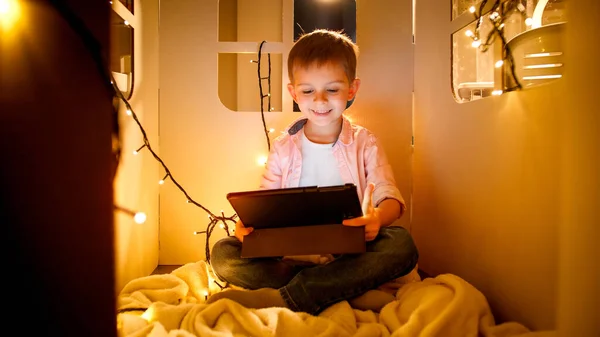 Felice ragazzo allegro sorridente guardare cartoni animati e giochi su tablet computer di notte. Concetto di educazione dei bambini e studio di notte — Foto Stock