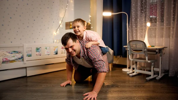 Alegre niño montando cerdito de nuevo en su padre por la noche. Concepto de niño jugando con los padres y la familia pasar tiempo juntos en la noche —  Fotos de Stock