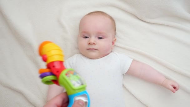 Aranyos kisfiú fekszik az ágyban, és nézi a színes játék által tartott szülő. A babaoktatás és -fejlesztés fogalma — Stock videók