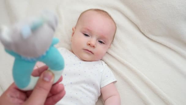 Ragazzino carino sdraiato nella culla e guardando i genitori scuotere giocattolo sonaglio. Concetto di educazione e sviluppo del bambino — Video Stock