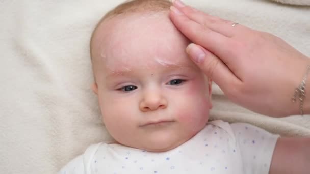 Großaufnahme einer Mutter, die Creme aufträgt, um ihre Babys zu befeuchten und ihr Gesicht zu reinigen. Konzept der Säuglingshygiene, Gesundheit und Hautpflege für Neugeborene — Stockvideo