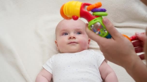 Jonge moeder schudden en spelen met kleurrijke plastic speelgoed met haar kleine baby liggend in wieg. — Stockvideo