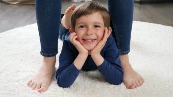 어머니 발 사이에 카펫 위에 누워 행복하게 미소짓고 있는 어린 소년의 모습 — 비디오