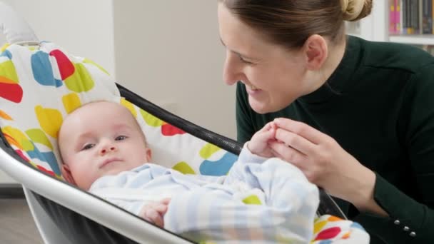 Portrait of smiling mother looking at her cute baby son sitting in electric rocking chair. Child development and happy parenting — Stock Video