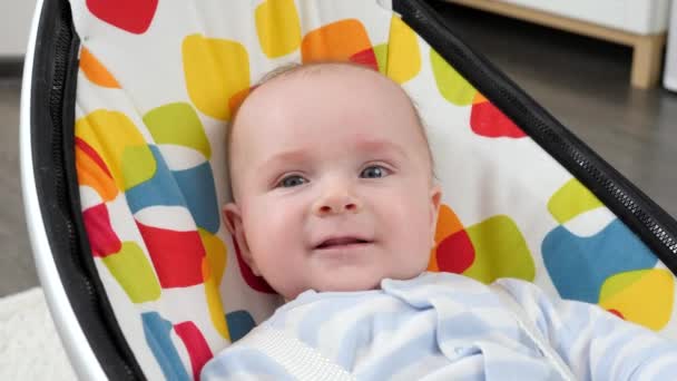 Portrait of smiling baby boy with blue eyes relaxing in electric rocking seat. Child development and happy childhood — Stock Video