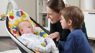 Mutlu erkek bebek oturma odasında oturan ailesinin yanındaki sandalyede sallanıyor. Çocuk gelişimi ve mutlu çocukluk