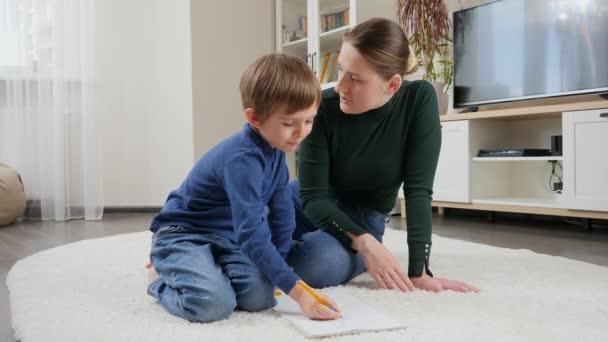 Madre joven regañando y gritando a su hijo haciendo la tarea en el suelo en la sala de estar. Concepto de problemas de educación doméstica, desarrollo infantil y paternidad — Vídeos de Stock