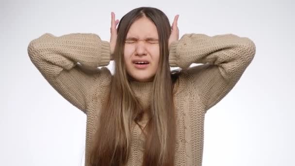 Раздраженная девушка с громким шумом закрывает уши руками на белом фоне студии — стоковое видео