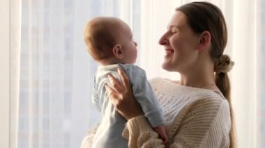 Mutlu gülümseyen anne oturma odasında küçük oğluna sarılıyor ve onu öpüyor. Aile mutluluğu ve ebeveynlik kavramı
