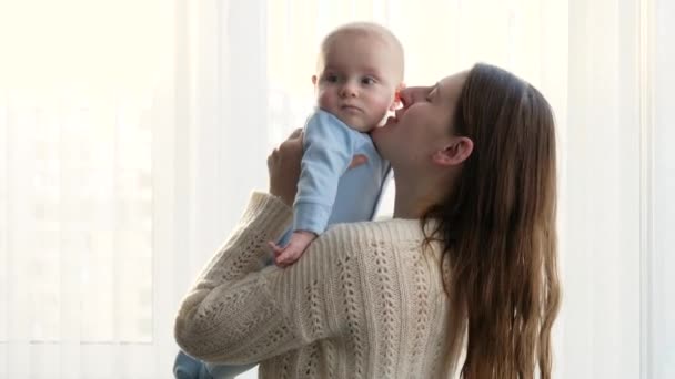 Mutlu gülümseyen anne, küçük oğlunu ellerinin arasına alıp kafasından öpüyor. Aile mutluluğu ve ebeveynlik kavramı — Stok video