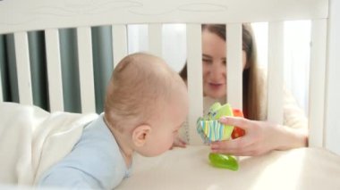 Anne beşikte oturup bebeğine oyuncak veriyor. Ebeveynlik kavramı, aile mutluluğu ve bebek gelişimi