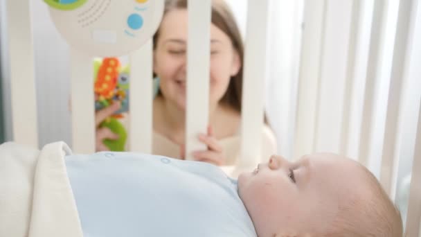 Portrait de jeune mère regardant à travers la rampe de berceau en bois sur son petit bébé couché dans le berceau. Concept de parentalité, bonheur familial et développement du bébé — Video