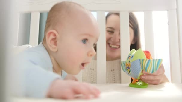 A kisbaba bölcsőben mászkál és színes játékokért nyúl. A szülőség, a család boldogsága és a baba fejlődése — Stock videók