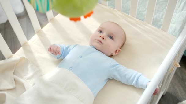 Schattige baby jongen liggend in wieg en op zoek naar kleurrijke schudden pluche speelgoed. Begrip ouderschap, gezinsgeluk en ontwikkeling van baby 's — Stockvideo