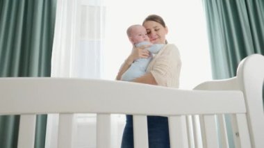 Mutlu gülümseyen anne, küçük oğluna sarılıyor ve onu öpüyor. Yatak odasında büyük bir pencereyle dikiliyor. Ebeveynlik kavramı, aile mutluluğu ve bebek gelişimi