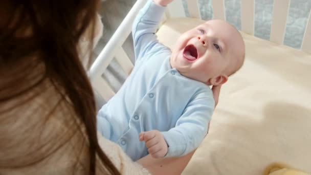 Χαρούμενο χαμογελαστό αγοράκι που κοιτάζει τη μητέρα του να τον κουνάει στην κούνια. Έννοια της γονικής μέριμνας, οικογενειακή ευτυχία και ανάπτυξη του μωρού — Αρχείο Βίντεο