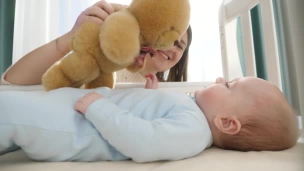 Kleiner Junge sucht und greift nach Teddybär in seiner Wiege. Konzept von Elternschaft, Familienglück und Babyentwicklung — Stockvideo