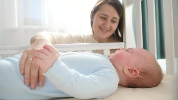 Porträt einer lächelnden Mutter, die neben der Wiege sitzt und ihren kleinen Sohn streichelt. Konzept von Elternschaft, Familienglück und Babyentwicklung — Stockvideo