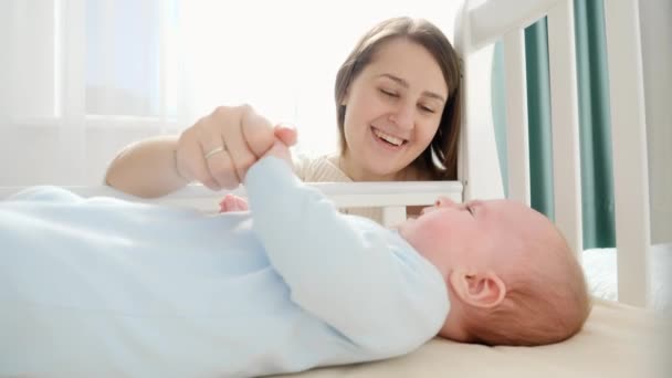 Lachende zorgzame en liefhebbende moeder streelde haar kleine baby in de wieg. Begrip ouderschap, gezinsgeluk en ontwikkeling van baby 's — Stockvideo